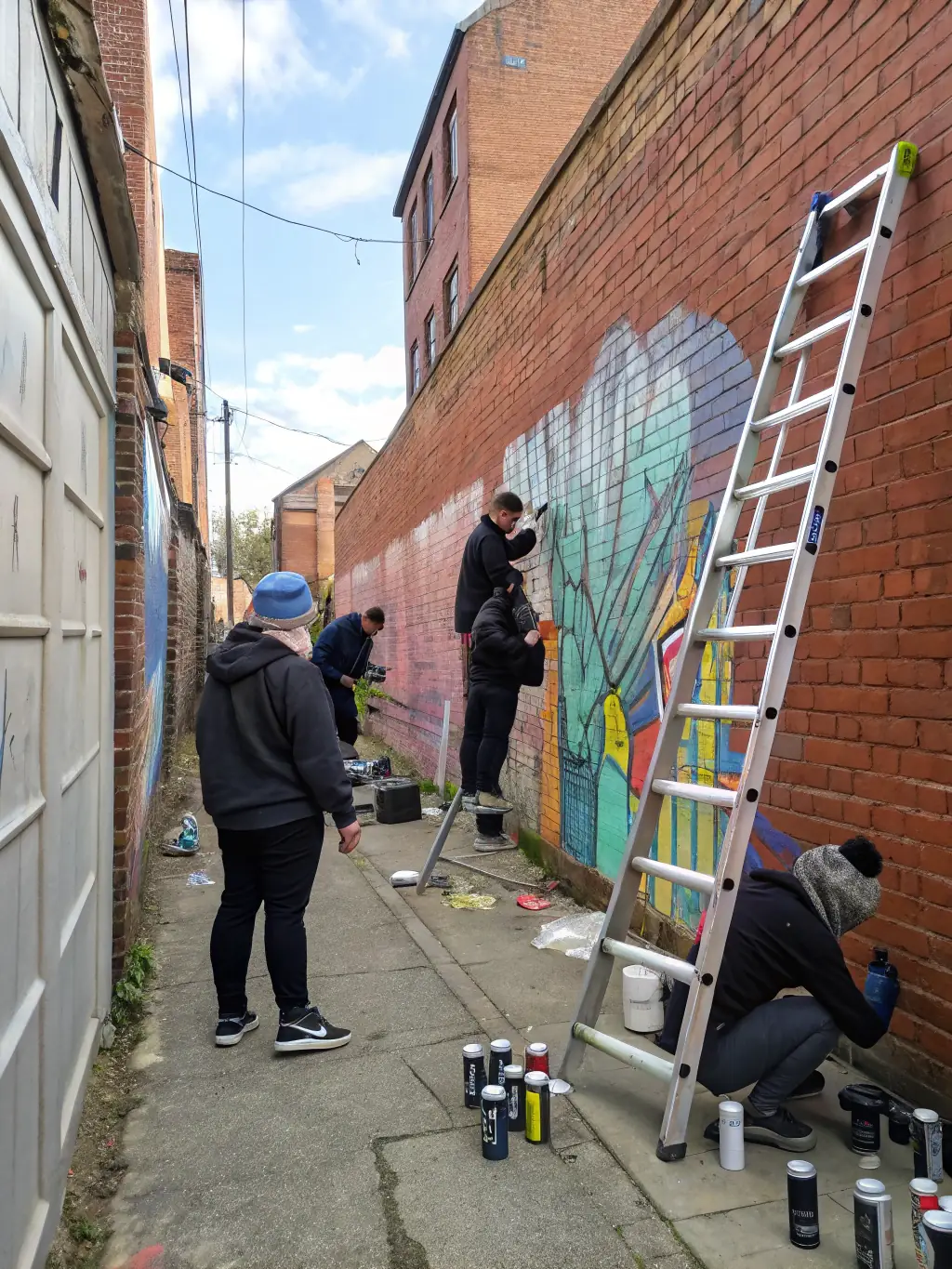 A photograph depicting a group of young artists participating in a collaborative mural painting project in a vibrant urban setting, showcasing the community art workshops offered by TOUT EN ART.